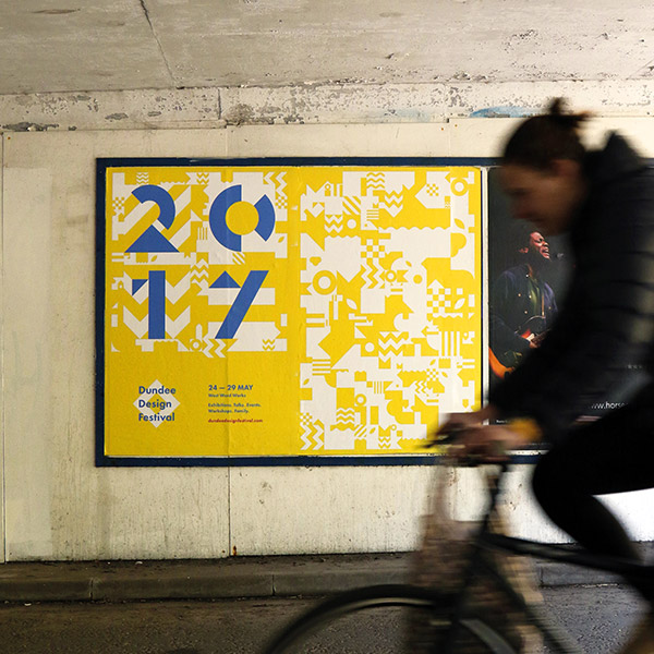 Blurred figure on a bike passes festival posters.