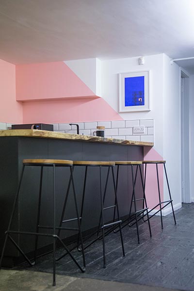 Matt black breakfast bar with three stools and a pink wall behind.
