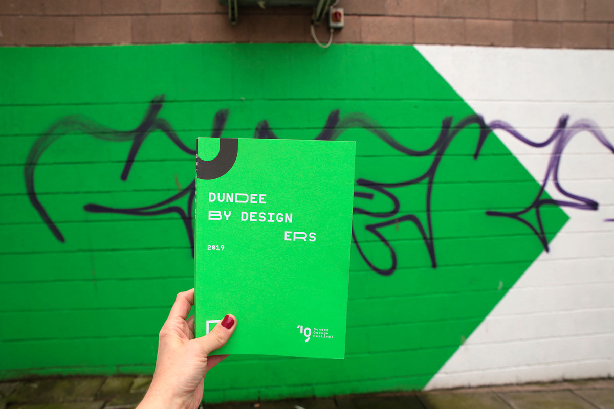 Bright green book help by a woman's hand in fornt of a colour matching wall.