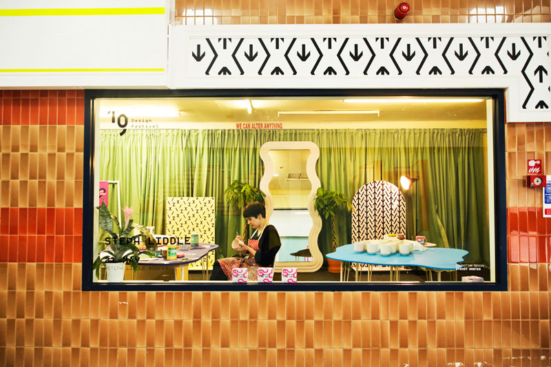 Woman works on hand decorating ceramics view is through a shop window.