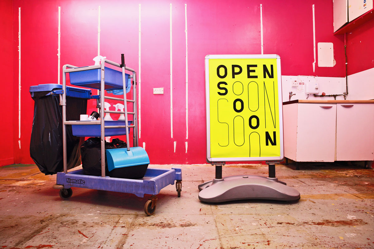 Deep pink room with luminous yellow sign with text that reads 'open soon'.