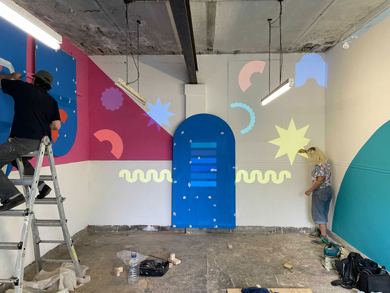 Two people are marking and painting the interior of the space the bold graphic shapes.