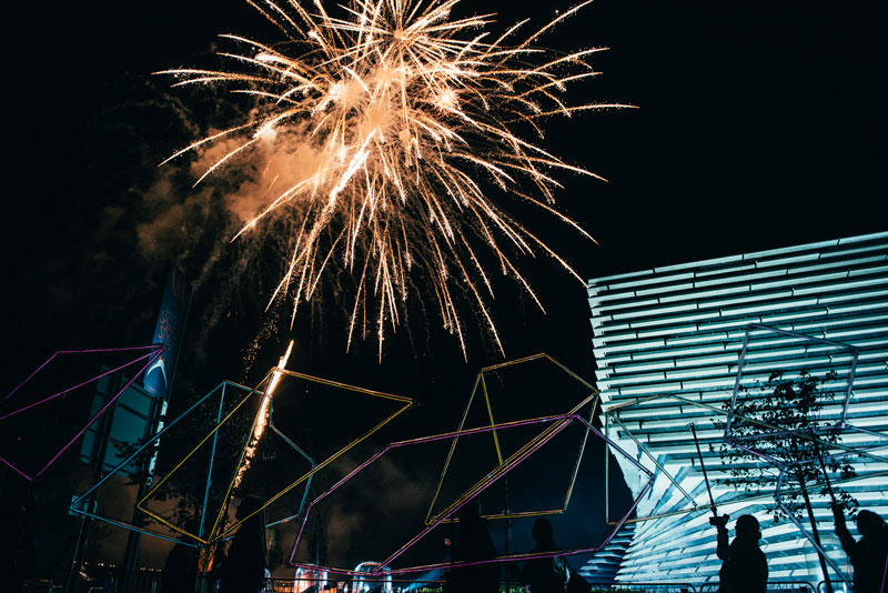 Giant illuminted shapes with fireworks in the background in fornt of V&A Dundee.