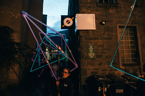 Giant illumintaed shapes being carried down an alley.